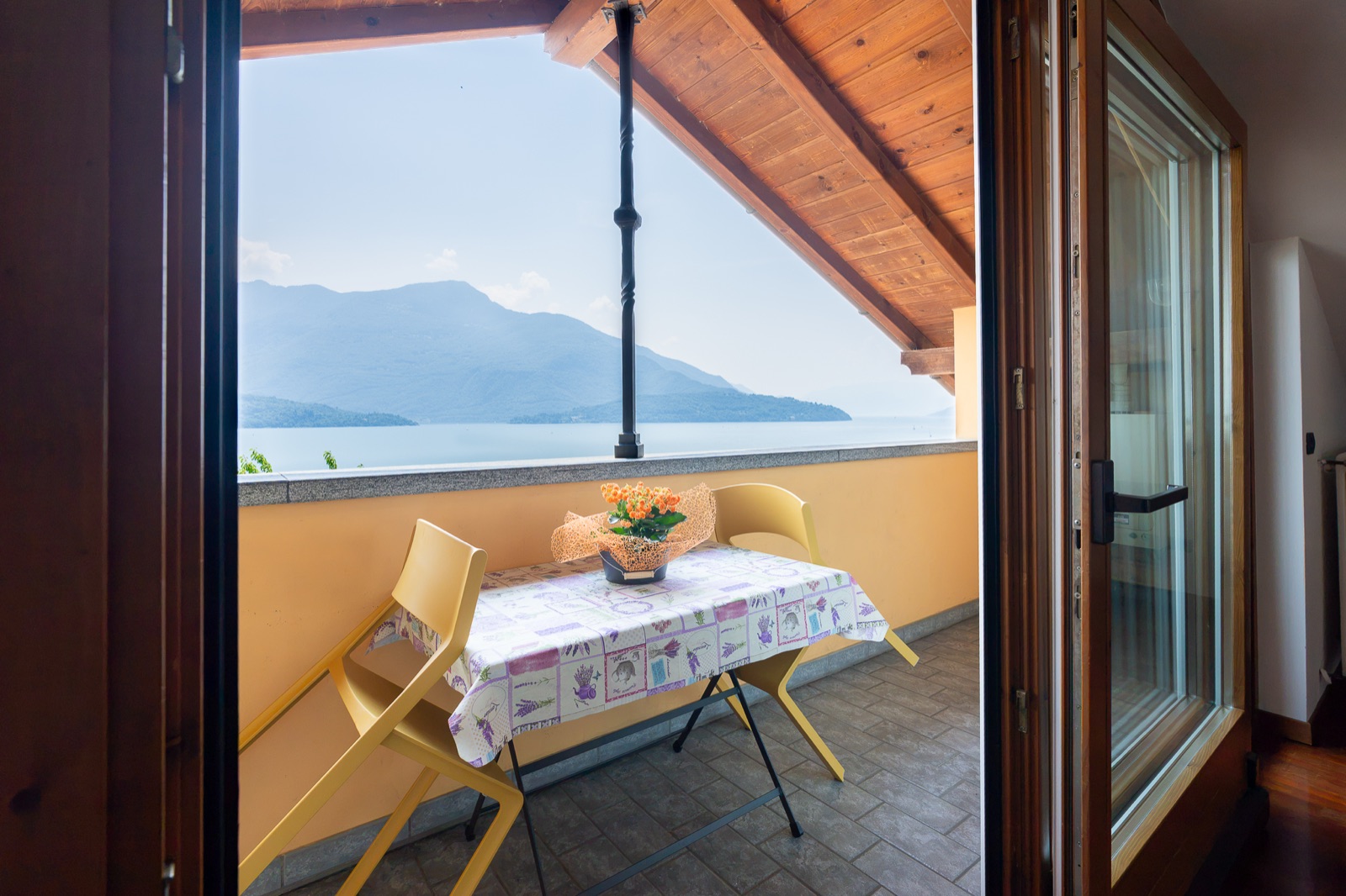Terrazza coperta con tavolino, sedie gialle e vista sul lago